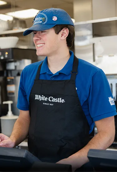 White Castle team member in black apron smiles while standing behind the restaurant counter.
