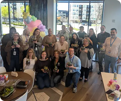 Group of employees holding small plants during a team celebration in a bright office space.