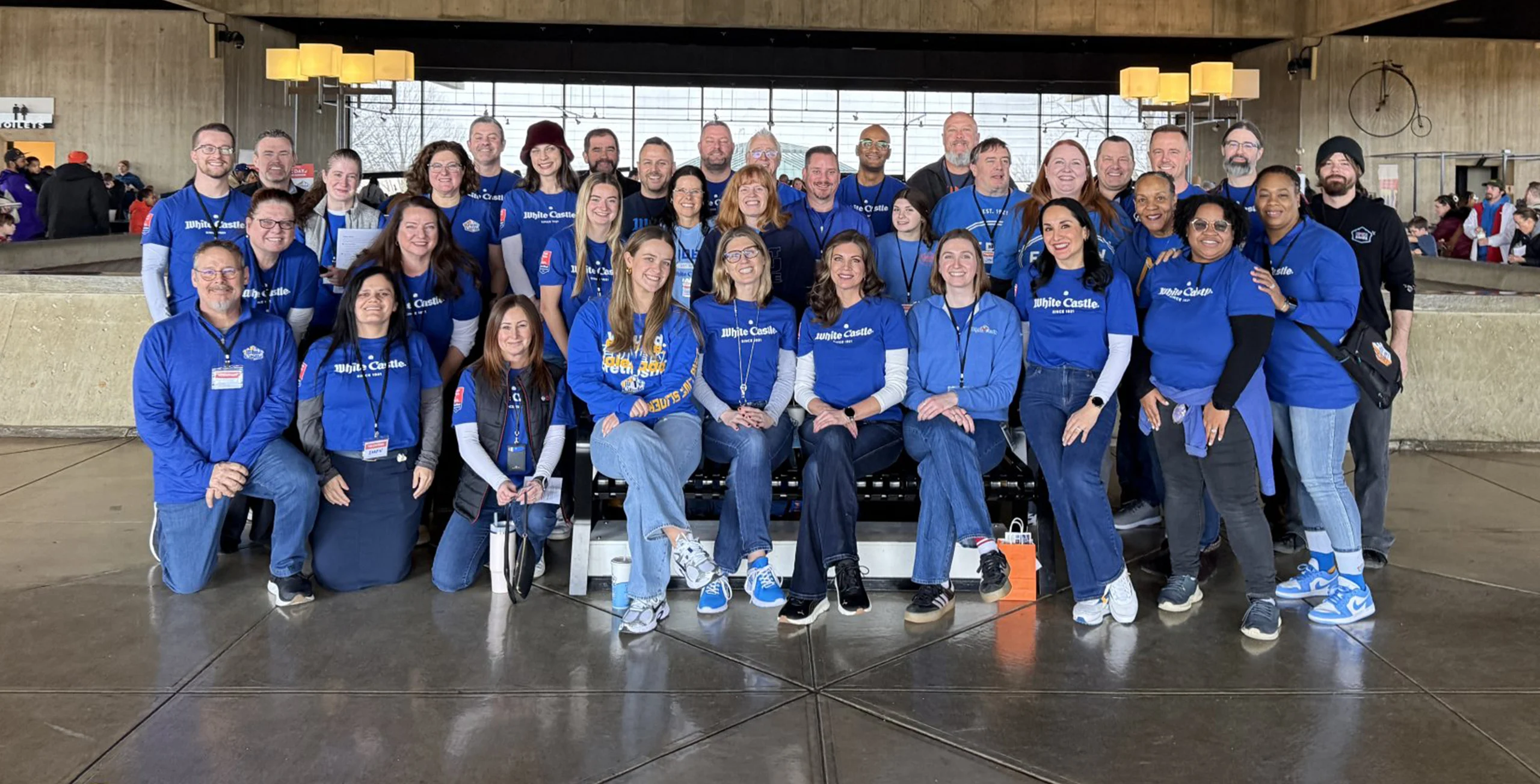 Large group of White Castle team members in blue shirts pose together for a group photo at an indoor event.